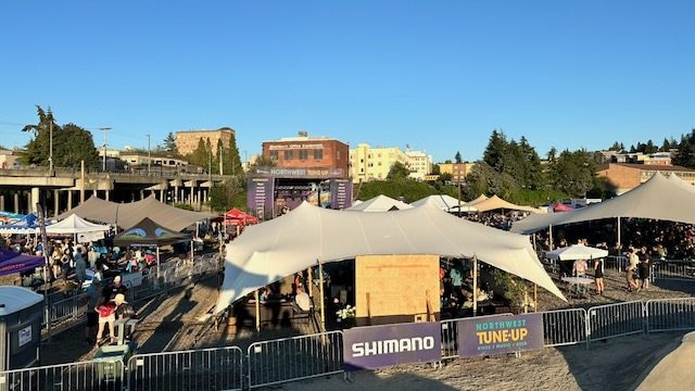 Daytime aerial view of the Northwest Tune-Up festival grounds in 2025, showing tents, a main stage, and crowds on the Trackside site with downtown Bellingham and the overpass in the background.